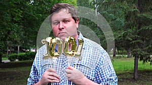Big man holding golden balloons making the 1001 number outdoor. 1001th anniversary celebration party