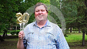 Big man holding golden balloons making the 20 number outdoor. 20th anniversary celebration party