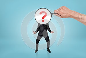 Big man's hand holding magnifying glass in front of question mark-headed businessman