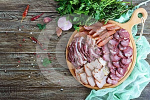 Big meat set. Homemade smoked pork-beef sausage, salted bacon, basturma chopped slices on a wooden board with spices and herbs.