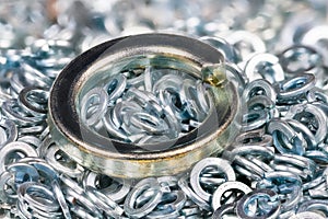 Big metal spring washer lying on heap of small stainless split washers blurry on background