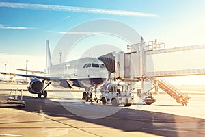 Big modern commercial plane on airfield docked with boarding bridge at sunrise or sunset. Blue clear sky on background. Travel and