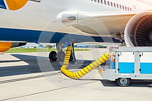 Big modern commercial plane parked on airport runway and connected to ground supply power unit. Aircraft maintenance