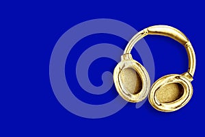 Big modern golden headphones isolated on blue background.