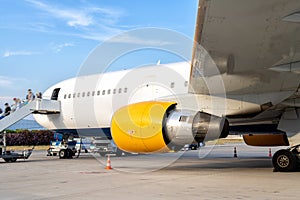 Big modern passenger airplane parked on airfield after arrival on bright sunny summer day. People disembark by plane ladder stairs