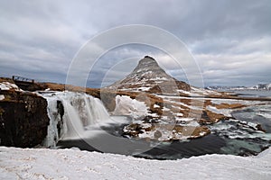 Big mountain in Iceland called Kirkjufell with a waterfall on a cloudy winter day.
