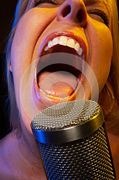 Big mouthed female vocalist under gelled lighting sings with passion into condenser microphone