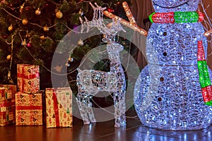 Big New Year`s Figures of a snowman, a deer and gifts from glowing multicolored garlands on the background of a decorated artific