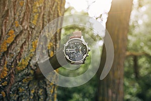 Big nice elegant men`s watch hanging on the tree in forest. Stylish fashion accessories outdoors