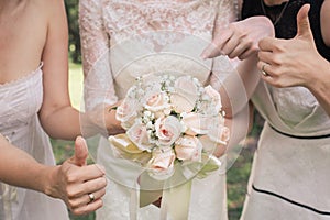 Big nice wedding bouquet in woman`s hands. Bride and bridesmaids show sign OK and thumbs up