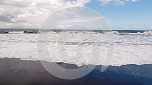 Big ocean waves breaking the shore of black volcanic beach. Slow motion.