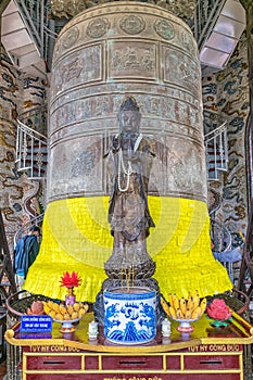 Big old metal bell with glued sheets with wishes and ancient statue in pagoda in Vietnam