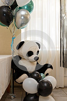 Big panda bear cuddly toy. Black, white, green and silver helium balloons for baby boy birthday party