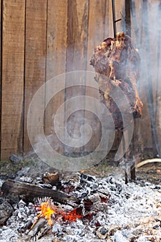 Piece of meat on skewer next to fire in the ground. Barbecue typical gaucho, leaving smoke and made with charcoal photo
