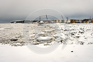 Big pieces of ice loosing and melting floes next to Port of Anchorage Small Boat Launch. Stevedore and cranes in the back.
