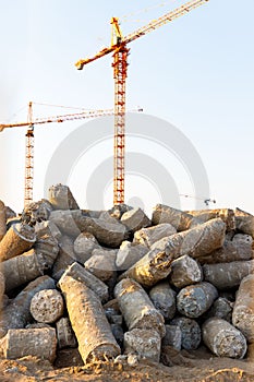 Big pile of cut concrete piles at construction site, tower cranes on background