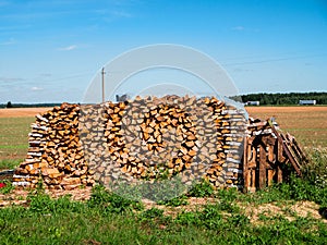 Big pile of fire wood in a field. Warm sunny day, blue sky. Traditional fuel for stove. Cost of living and business