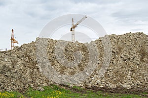 A big pile of land near the construction site. There`s clay in there. Construction cranes are visible at the back of the