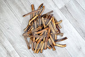 Big pile of sticks of dried beef pizzles of different sizes, big and small, lying down on wooden white background.