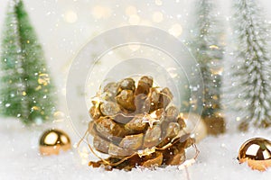 Big pine cone with golden garland lights in winter scene in forest with fir trees falling snow. Christmas New Years holiday magic