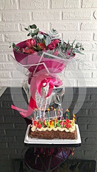 Big pink beautiful festive gift bouquet of flowers for a birthday and a cake with burning candles on the table against the