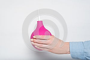 Big pink enema in a female hand. White background. Medical item