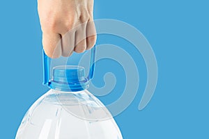 Big plastic bottle with water in hand, clean drinking water on a blue background, copy space