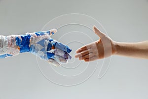 Big plastic hand made of garbage shaking another hand isolated on white studio background