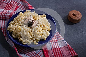 Big portion of pasta with fish on blue plate, red towel, grey background. Macaroni with pilchard or sardine. Overeating