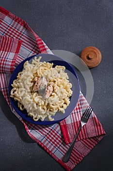 Big portion of pasta with fish on blue plate, red towel, grey background. Macaroni with pilchard or sardine. Top view, vertical
