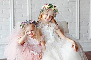 Big portrait of two cute funny and beauty little girl - sisters in wreaths of fresh flowers and lush pink elegant dresses laugh