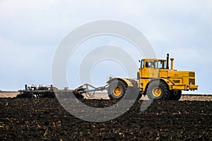 Big powerful wheeled yellow tractor pulls the disc harrow plowing the field