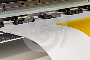 Big professional printer, processing a large scale glossy sheet of yellow paper rolls for color sampling.