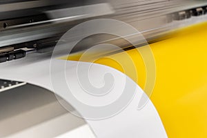 Big professional printer, processing a large scale glossy sheet of yellow paper rolls for color sampling.