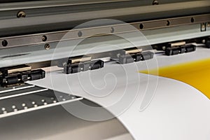 Big professional printer, processing a large scale glossy sheet of yellow paper rolls for color sampling.