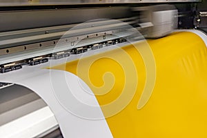 Big professional printer, processing a large scale glossy sheet of yellow paper rolls for color sampling.