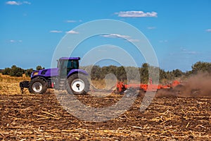 Big purple tractor plows the field and removes the remains of previously mown sunflower.