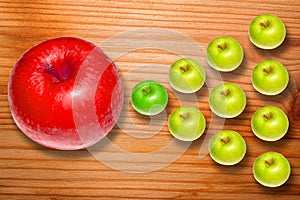 Big red apple and group of ordered green apples on wooden desk