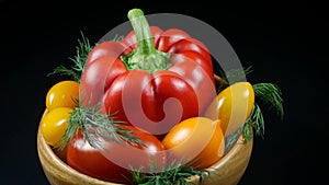 A big red bell pepper, four yellow tomatoes, one red tomato and dill twigs are in a round brown wooden bowl