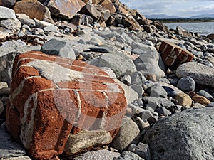 Big red brick boulder block on a rocky beach waterfront