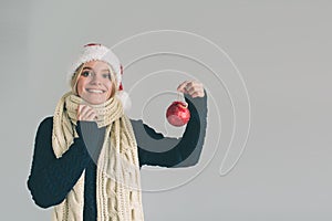 Big red Christmas ball in hands at the women. The girl is dressed in sweater, christmas hat and scarf studio shot