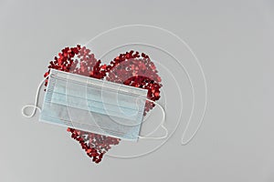 Big red heart made from little glittering confeti partly covered with medical mask, protective measures on valentines day, new rea photo