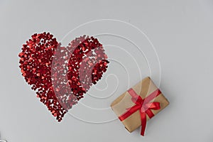 Big red heart made from little glittering confeti of heart shapes, gift box with red ribbon is near, photo