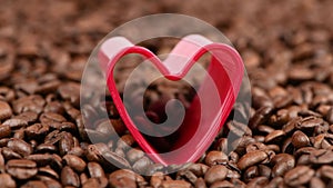 Big red heart on roasted coffee beans. The concept of coffee adoration. Side view.