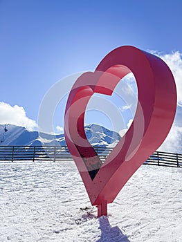 a big red metal heart in the middle of a ski slope, with snowy mountains, passion for skiing, winter sport, valentines day, copy