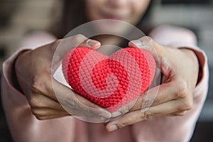 Big red yarn heart holding and giving to front by woman hand. Love and affection in Valentines day concept. Romantic object and