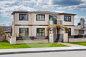 Big residential house with fence and gate in front on cloudy day