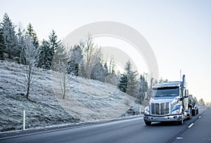 Big rig American semi truck with tank semi trailer transporting liquid cargo on the winter road with frost on the hill