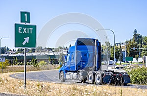 Big rig blue bonnet semi truck tractor turning on the highway exit running to warehouse for pick up loaded semi trailer for the