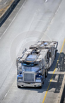 Big rig blue car hauler semi truck with empty semi trailer running on the road to warehouse for loading cars